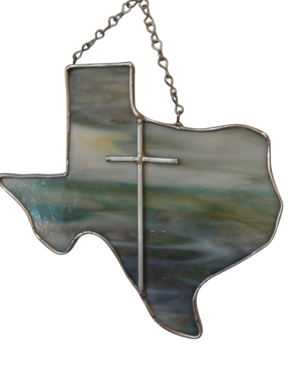 Stained glass in the shape of Texas with a cross, made from soft green and blue glass.